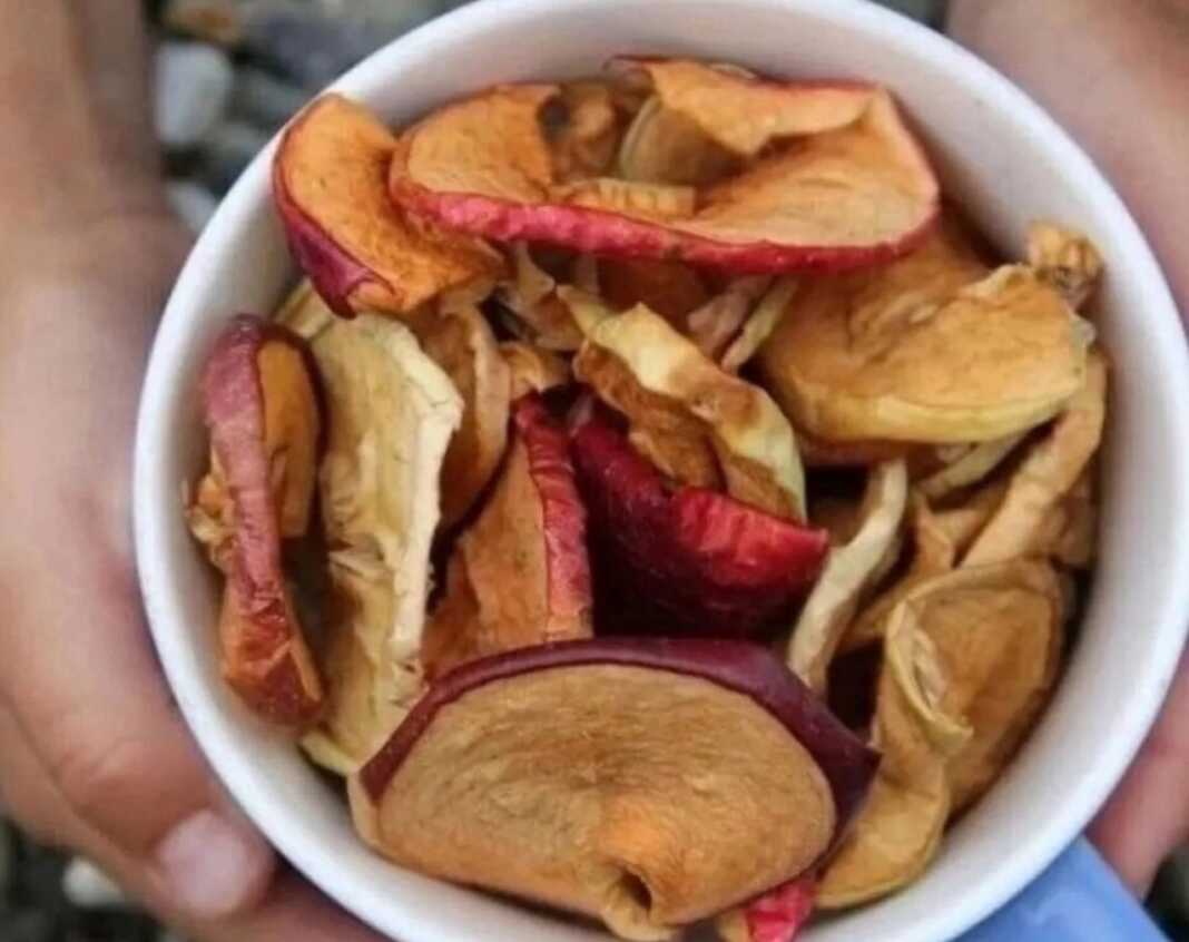 Φέτες αποξηραμένων μήλων τοποθετημένες σε ένα ξύλινο μπολ, έτοιμες για κατανάλωση ως υγιεινό σνακ.