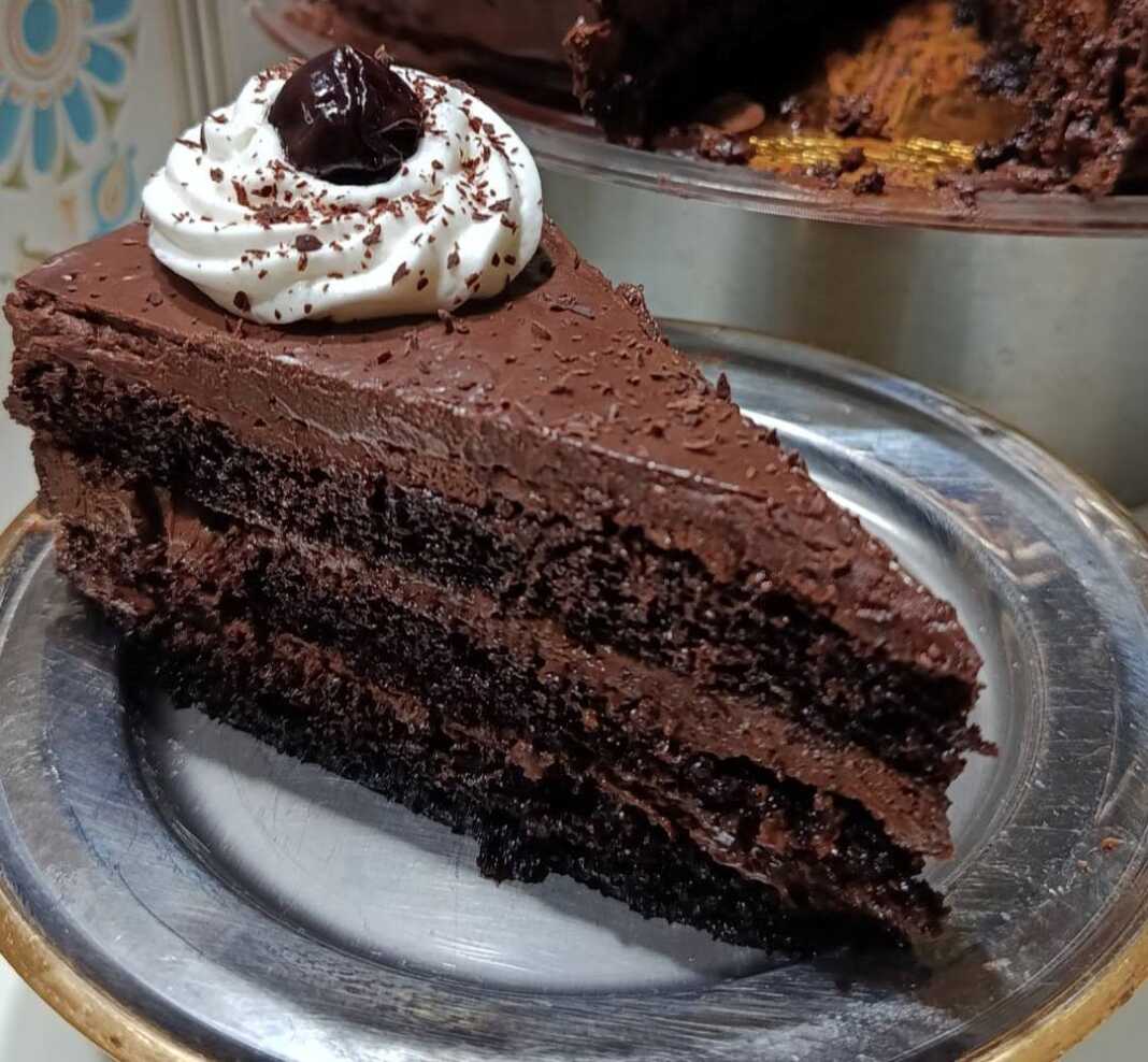 Μια επιβλητική τούρτα Μπλάκ Φόρεστ καλυμμένη με γκανάζ σοκολάτας, ροζέτες σαντιγί και ολόκληρα βύσσινα.