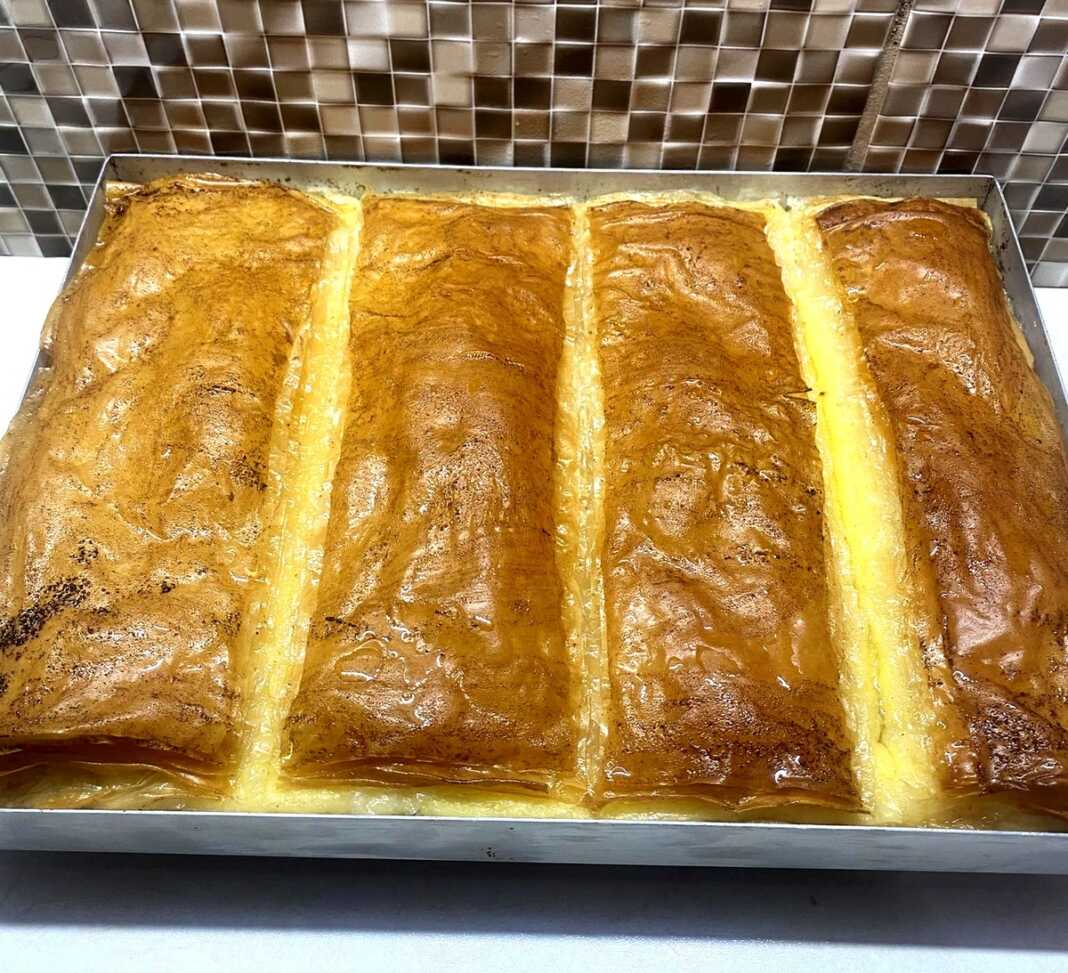 Ταψί με χρυσαφένιο, σιροπιασμένο γαλακτομπούρεκο κομμένο σε τετράγωνα κομμάτια.