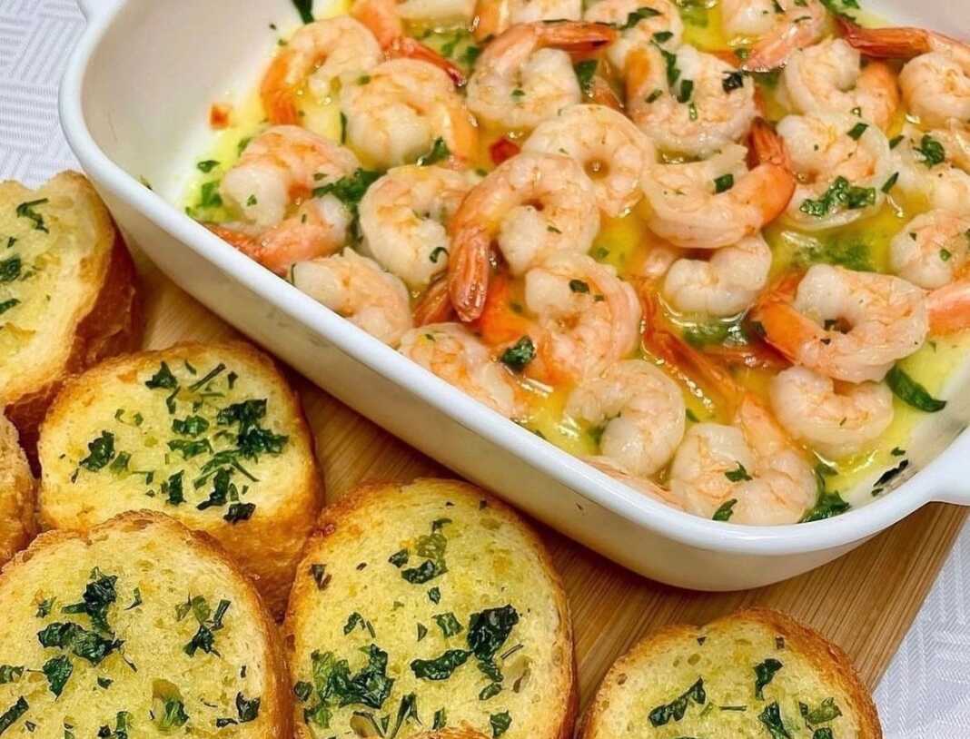 Ζουμερές γαρίδες στον φούρνο μέσα σε πλούσιο σκορδοβούτυρο, γαρνιρισμένες με φρέσκα μυρωδικά και φέτες λεμονιού