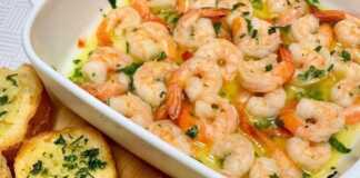 Ζουμερές γαρίδες στον φούρνο μέσα σε πλούσιο σκορδοβούτυρο, γαρνιρισμένες με φρέσκα μυρωδικά και φέτες λεμονιού