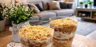 Δύο κομψά ποτήρια γεμάτα με στρώσεις από τριμμένο μπισκότο, κρέμα και πουρέ μπανάνας, διακοσμημένα με λίγα ψίχουλα μπισκότου στην κορυφή.