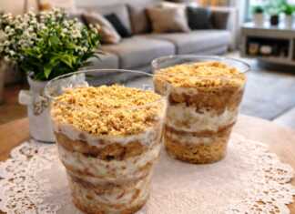 Δύο κομψά ποτήρια γεμάτα με στρώσεις από τριμμένο μπισκότο, κρέμα και πουρέ μπανάνας, διακοσμημένα με λίγα ψίχουλα μπισκότου στην κορυφή.