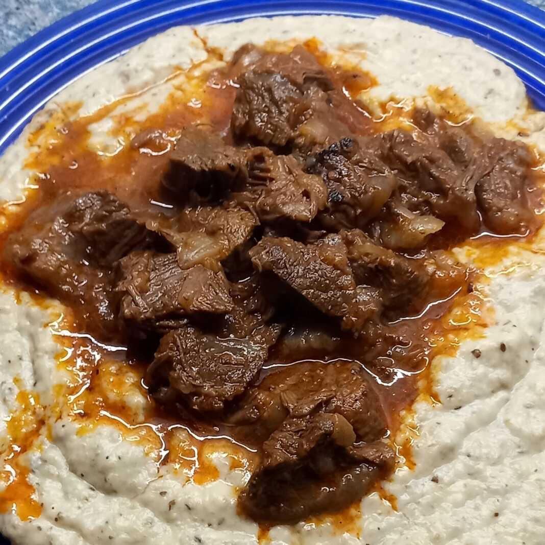 Ένα πλούσιο πιάτο Χουνκιάρ Μπεγιεντί με τρυφερό κοκκινιστό μοσχάρι πάνω σε βελούδινο λευκό πουρέ μελιτζάνας, γαρνιρισμένο με φρέσκο μαϊντανό.