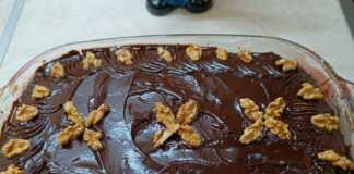 Ένα κομμάτι σιροπιαστή καρυδόπιτα με πλούσια επικάλυψη σοκολάτας, σερβιρισμένο σε πιάτο με λίγα καρύδια δίπλα.