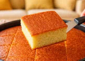 Ένα ψηλό και αφράτο κέικ γάλακτος σε ανοιχτόχρωμο χρυσό χρώμα, κομμένο σε τετράγωνα κομμάτια πάνω σε μια σχάρα.