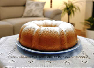 Ένα χρυσαφένιο αφράτο κέικ καρότου πασπαλισμένο με άχνη ζάχαρη πάνω σε μια μεταλλική σχάρα.