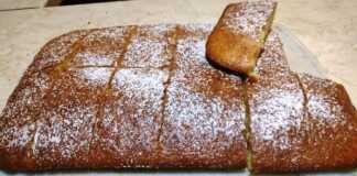 Κλασικό Κέικ: Η Διαχρονική Αξία της Απλότητας στο Τραπέζι σας! Ένα φρεσκοψημένο χρυσαφένιο κέικ ταψιού πασπαλισμένο με λευκή ζάχαρη άχνη, κομμένο σε τετράγωνα κομμάτια.