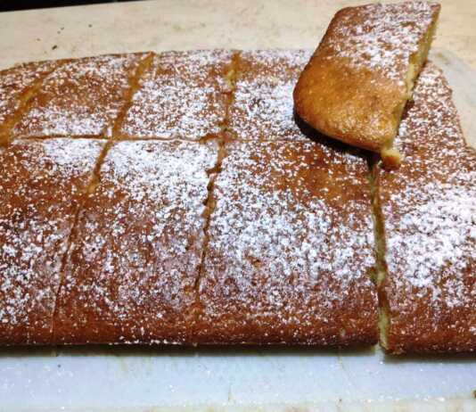 Ένα φρεσκοψημένο χρυσαφένιο κέικ ταψιού πασπαλισμένο με λευκή ζάχαρη άχνη, κομμένο σε τετράγωνα κομμάτια.