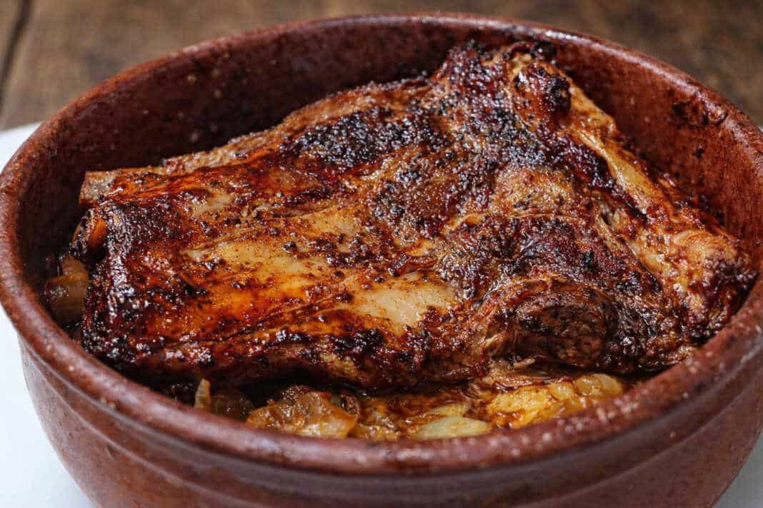 Σιγομαγειρεμένη χοιρινή κορτεζίνα μέσα σε πήλινο σκεύος, με πλούσια σκούρα σάλτσα και αρωματικά κρεμμύδια.