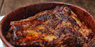 Σιγομαγειρεμένη χοιρινή κορτεζίνα μέσα σε πήλινο σκεύος, με πλούσια σκούρα σάλτσα και αρωματικά κρεμμύδια.