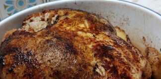 Κοτόπουλο Γεμιστό με Ρυζάκι: Η Επιτομή της Σπιτικής Θαλπωρής στο Πιάτο σας! Ένα ολόκληρο ροδοκοκκινισμένο κοτόπουλο γεμιστό με ρύζι, περιτριγυρισμένο από μελωμένες πατάτες baby μέσα σε ένα κεραμικό πλακερό.