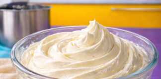 Ένα μπολ με λευκή, πλούσια και σταθερή κρέμα βουτύρου που έχει σχηματίσει κορυφές, έτοιμη για διακόσμηση.