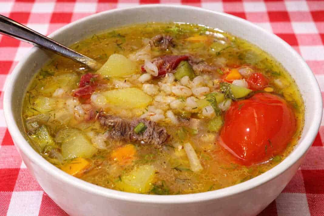 Ένα βαθύ πιάτο με ζεστή χωριάτικη σούπα από κριθάρι και κομμάτια τουρσί, σερβιρισμένη με φρέσκο ψωμί.