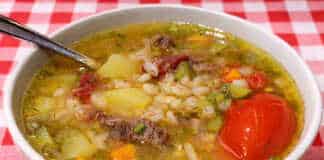 Ένα βαθύ πιάτο με ζεστή χωριάτικη σούπα από κριθάρι και κομμάτια τουρσί, σερβιρισμένη με φρέσκο ψωμί.