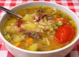 Ένα βαθύ πιάτο με ζεστή χωριάτικη σούπα από κριθάρι και κομμάτια τουρσί, σερβιρισμένη με φρέσκο ψωμί.