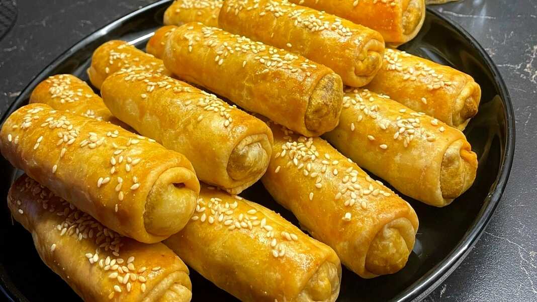 Μικρές ροδοκοκκινισμένες λαχανόπιτες Σαρακοστής αλειμμένες με αυγό και πασπαλισμένες με σουσάμι πάνω σε λαδόκολλα