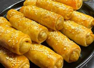 Μικρές ροδοκοκκινισμένες λαχανόπιτες Σαρακοστής αλειμμένες με αυγό και πασπαλισμένες με σουσάμι πάνω σε λαδόκολλα