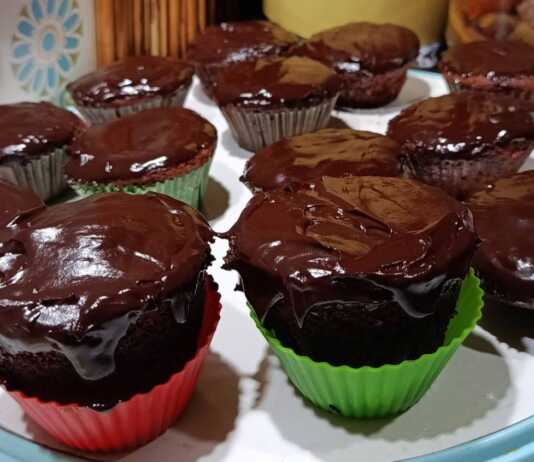 Αφράτα μάφιν πορτοκαλιού με επικάλυψη γυαλιστερού γλάσου σοκολάτας, τοποθετημένα σε μια βάση σερβιρίσματος.