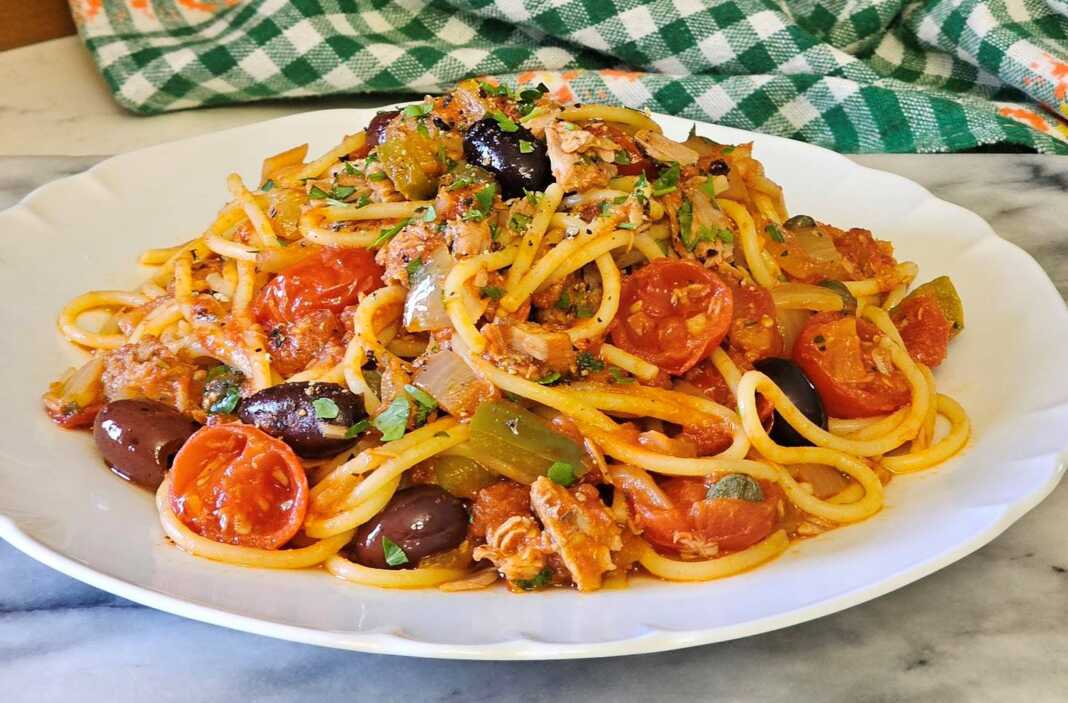 Μια αχνιστή μακαρονάδα με τόνο, κόκκινη σάλτσα, ελιές και φρέσκο βασιλικό σε λευκό πιάτο