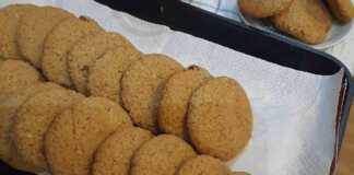 Μια πιατέλα με χρυσαφένια σπιτικά μπισκότα βρώμης, πασπαλισμένα με λίγη κανέλα και δίπλα μερικές νιφάδες βρώμης και σταφίδες.