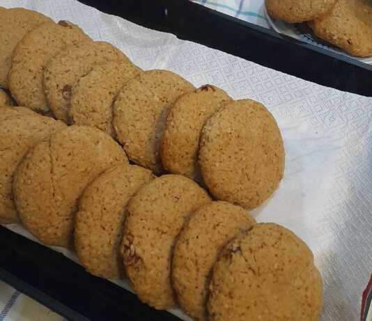 Μια πιατέλα με χρυσαφένια σπιτικά μπισκότα βρώμης, πασπαλισμένα με λίγη κανέλα και δίπλα μερικές νιφάδες βρώμης και σταφίδες.