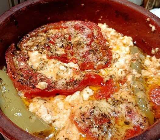 Ένα πήλινο σκεύος με λιωμένη φέτα, ντομάτα και καυτερή πιπεριά, πασπαλισμένο με μπόλικη ρίγανη.