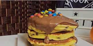 Μια στοίβα από λαχταριστά χρυσαφένια πάνκεικς με πορτοκάλι, περιχυμένα με πλούσια πραλίνα σοκολάτας και πολύχρωμα καραμελάκια.