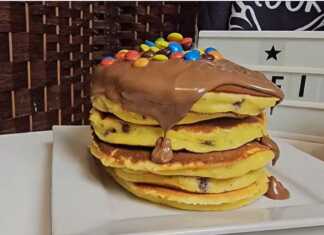 Μια στοίβα από λαχταριστά χρυσαφένια πάνκεικς με πορτοκάλι, περιχυμένα με πλούσια πραλίνα σοκολάτας και πολύχρωμα καραμελάκια.