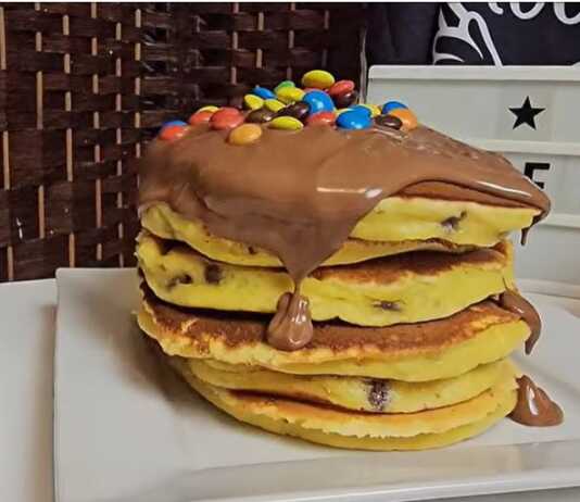 Μια στοίβα από λαχταριστά χρυσαφένια πάνκεικς με πορτοκάλι, περιχυμένα με πλούσια πραλίνα σοκολάτας και πολύχρωμα καραμελάκια.