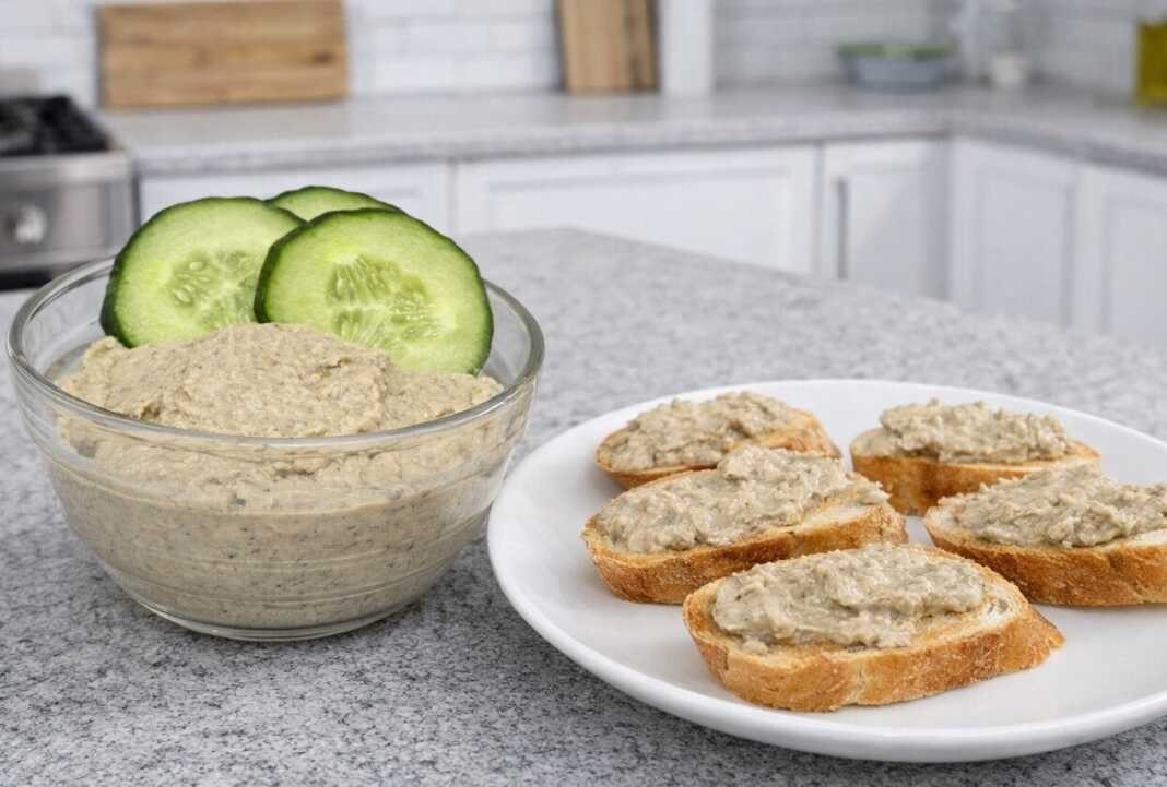 Ένα μπολ με βελούδινο πατέ μελιτζάνας γαρνιρισμένο με ολόκληρα καρύδια και φρέσκα μυρωδικά.