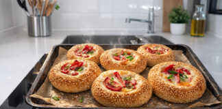 Αφράτα μίνι ψωμάκια πίτσας με σουσάμι ζαμπόν τυρί και πιπεριά τοποθετημένα σε σειρά πάνω σε λαδόκολλα