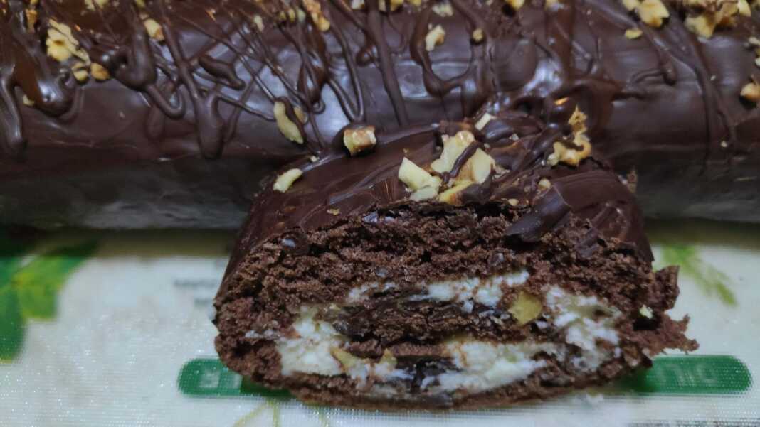 Ένα λαχταριστό ρολό σοκολάτας καλυμμένο με γλάσο και πασπαλισμένο με καβουρδισμένους ξηρούς καρπούς, κομμένο σε φέτες.