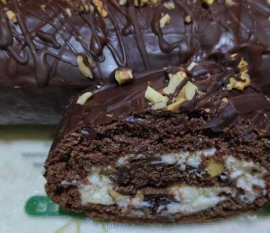 Ένα λαχταριστό ρολό σοκολάτας καλυμμένο με γλάσο και πασπαλισμένο με καβουρδισμένους ξηρούς καρπούς, κομμένο σε φέτες.