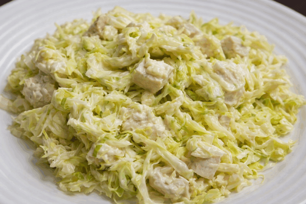 Μια μεγάλη σαλατιέρα με ψιλοκομμένο λάχανο, κομμάτια στήθος κοτόπουλο και κρεμώδη σως γιαουρτιού.