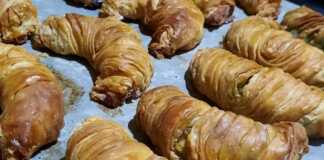 Σπανακοτυροπιτάκια στριφτά: το πιο τραγανό φύλλο που έγινε ποτέ Σειρές από ροδοκοκκινισμένα σπανακοτυροπιτάκια στριφτά μέσα στο ταψί, αλειμμένα με αυγό για λάμψη