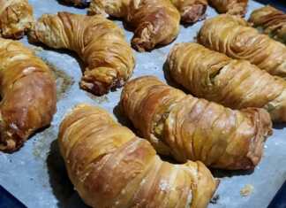 Σειρές από ροδοκοκκινισμένα σπανακοτυροπιτάκια στριφτά μέσα στο ταψί, αλειμμένα με αυγό για λάμψη