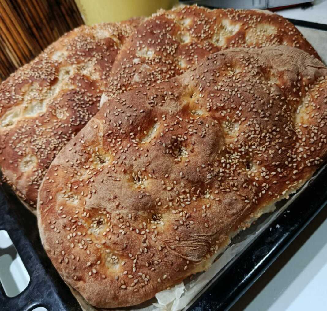 Δύο μεγάλες παραδοσιακές λαγάνες με δαχτυλιές και άφθονο σουσάμι πάνω σε λαδόκολλα μόλις βγήκαν από τον φούρνο