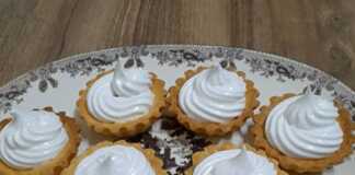 Ταρτάκια με Μαρέγκα: Η Αέρινη Γλυκιά Πολυτέλεια στο Πιάτο σας! Σειρά από χρυσαφένια ταρτάκια γεμισμένα με κόκκινη μαρμελάδα και ψηλές κορυφές λευκής μαρέγκας.