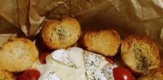 Ένα στρογγυλό ταψάκι με λιωμένο τυρί Brie στο κέντρο, περιτριγυρισμένο από ψητά ντοματίνια και τραγανές φέτες μπαγκέτας.