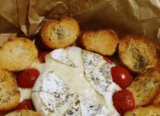 Ένα στρογγυλό ταψάκι με λιωμένο τυρί Brie στο κέντρο, περιτριγυρισμένο από ψητά ντοματίνια και τραγανές φέτες μπαγκέτας.