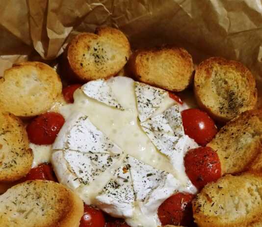 Ένα στρογγυλό ταψάκι με λιωμένο τυρί Brie στο κέντρο, περιτριγυρισμένο από ψητά ντοματίνια και τραγανές φέτες μπαγκέτας.