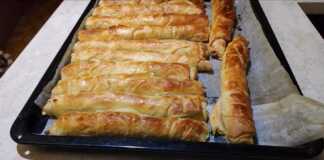 Σειρές από ροδοκοκκινισμένες χειροποίητες τυρόπιτες με σφολιάτα πάνω σε ταψί με λαδόκολλα.