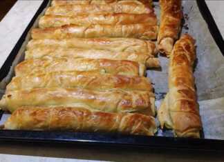 Σειρές από ροδοκοκκινισμένες χειροποίητες τυρόπιτες με σφολιάτα πάνω σε ταψί με λαδόκολλα.