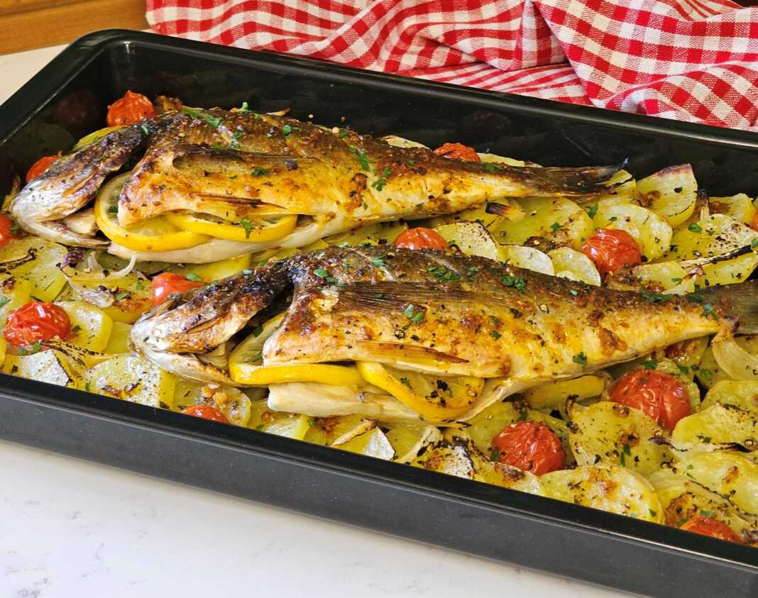 Δύο ολόκληρες τσιπούρες ψημένες στο φούρνο πάνω σε ένα στρώμα από ροδέλες πατάτας και κρεμμυδιού, περιτριγυρισμένες από ζουμερά ντοματίνια.