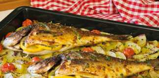 Δύο ολόκληρες τσιπούρες ψημένες στο φούρνο πάνω σε ένα στρώμα από ροδέλες πατάτας και κρεμμυδιού, περιτριγυρισμένες από ζουμερά ντοματίνια.