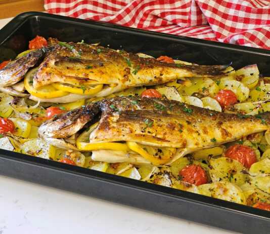 Δύο ολόκληρες τσιπούρες ψημένες στο φούρνο πάνω σε ένα στρώμα από ροδέλες πατάτας και κρεμμυδιού, περιτριγυρισμένες από ζουμερά ντοματίνια.