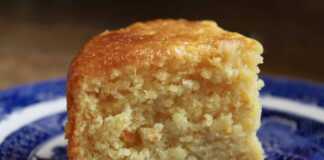 Ένα ζουμερό σιροπιαστό κέικ πορτοκαλιού σε φόρμα, γαρνιρισμένο με φρέσκο ξύσμα, έτοιμο για σερβίρισμα.