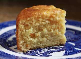 Ένα ζουμερό σιροπιαστό κέικ πορτοκαλιού σε φόρμα, γαρνιρισμένο με φρέσκο ξύσμα, έτοιμο για σερβίρισμα.