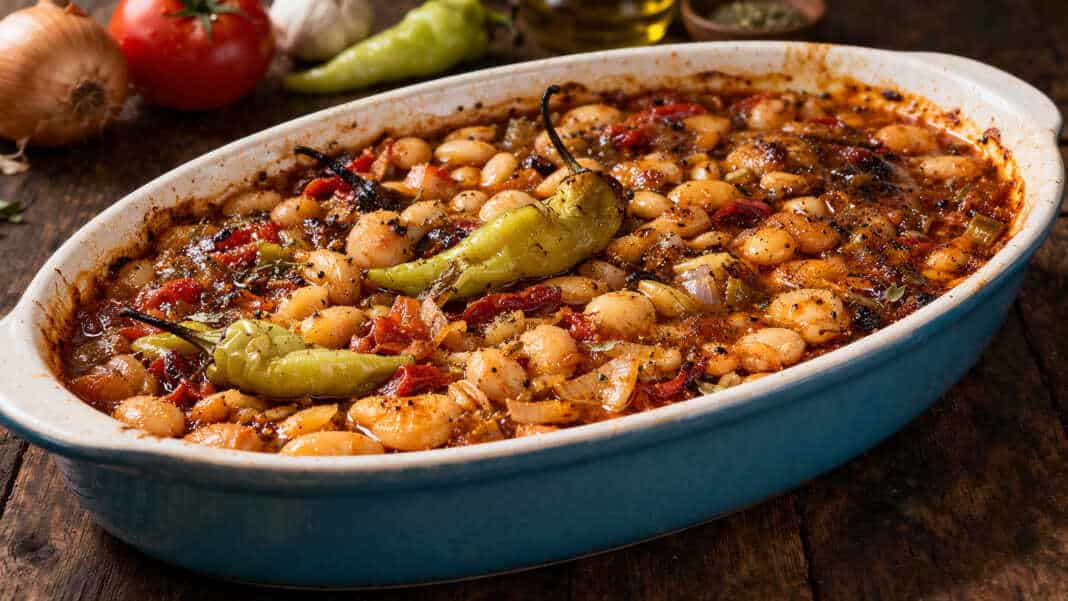 Καλοψημένα φασόλια μέσα σε ταψί με πλούσια κόκκινη σάλτσα, κομμάτια πράσου, καρότου και ολόκληρες καυτερές πιπεριές